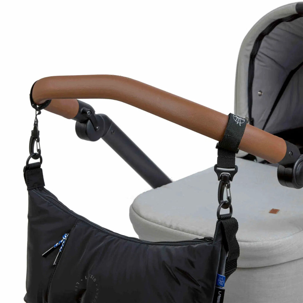 LÄSSIG lunua diaper bag black attached to stroller with brown leather handle and black straps