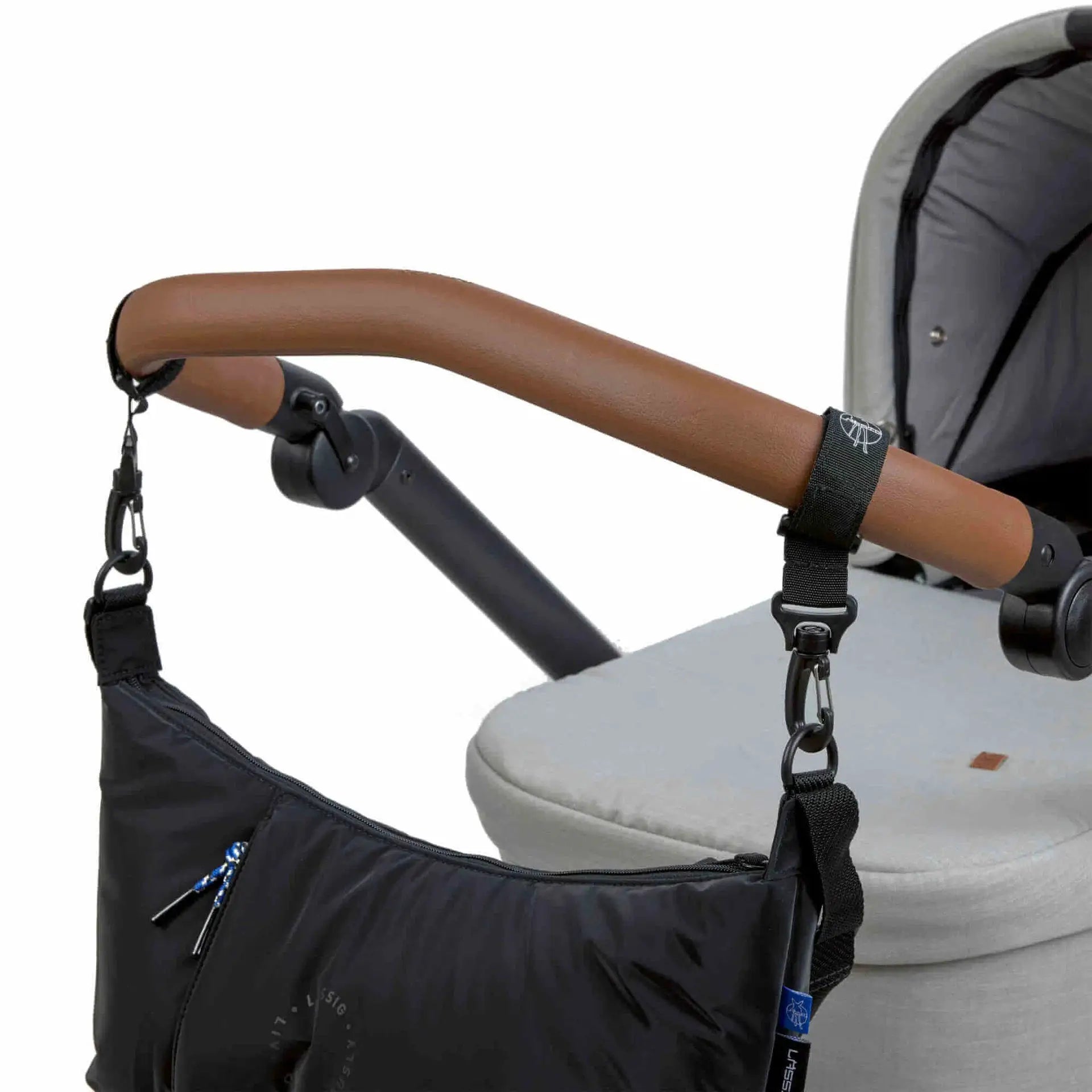 LÄSSIG lunua diaper bag black attached to stroller with brown leather handle and black straps