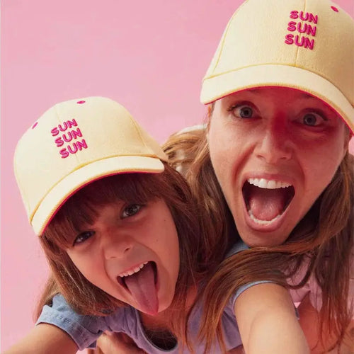 CHAMAYE baseball caps; two pale yellow caps with pink SUN embroidery against a pink background.