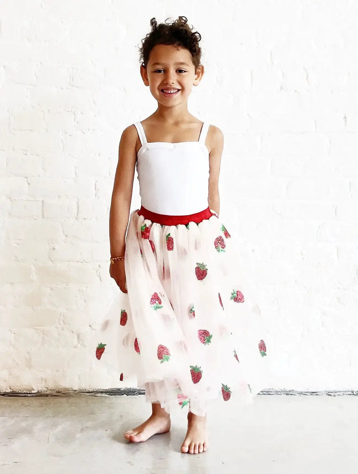 Long strawberry-print tutu skirt with red waistband worn by a girl in a white top