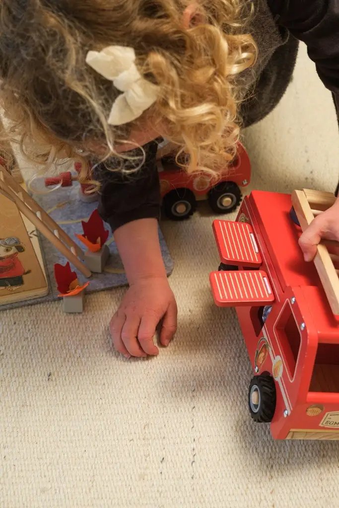 Camion de pompiers jouet rouge EGMONT TOYS sur tapis, enfant jouant à côté
