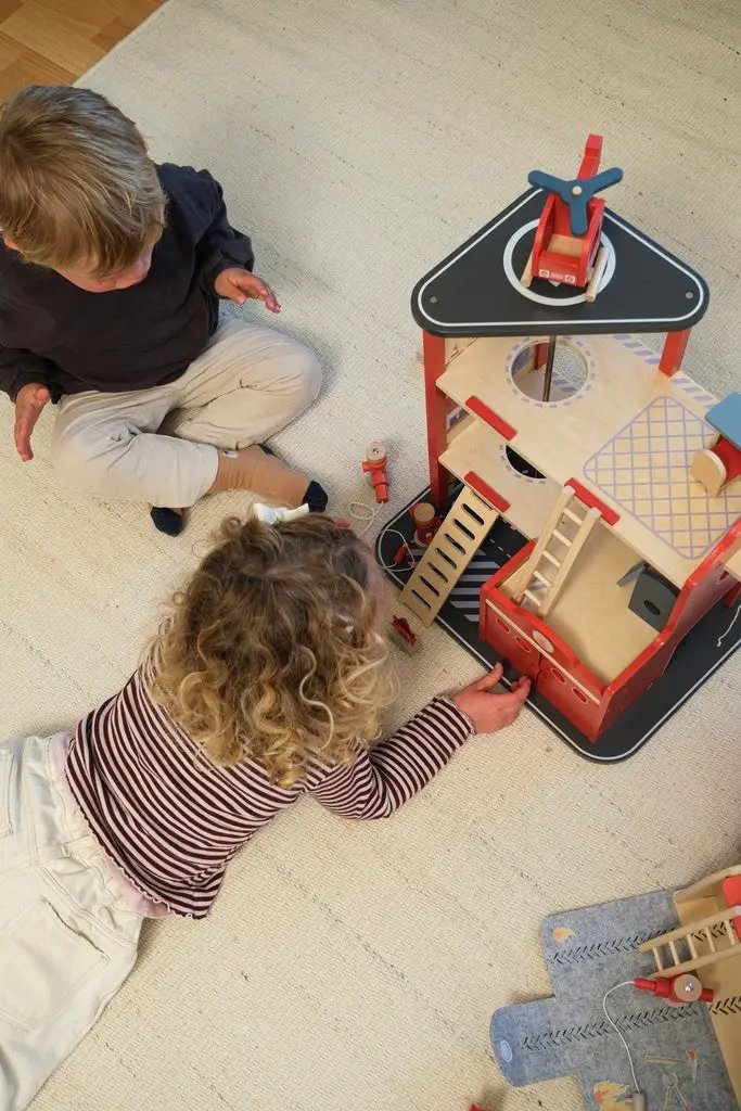 EGMONT TOYS caserne des pompiers wooden fire station set, red and natural wood with ladders; two kids playing.