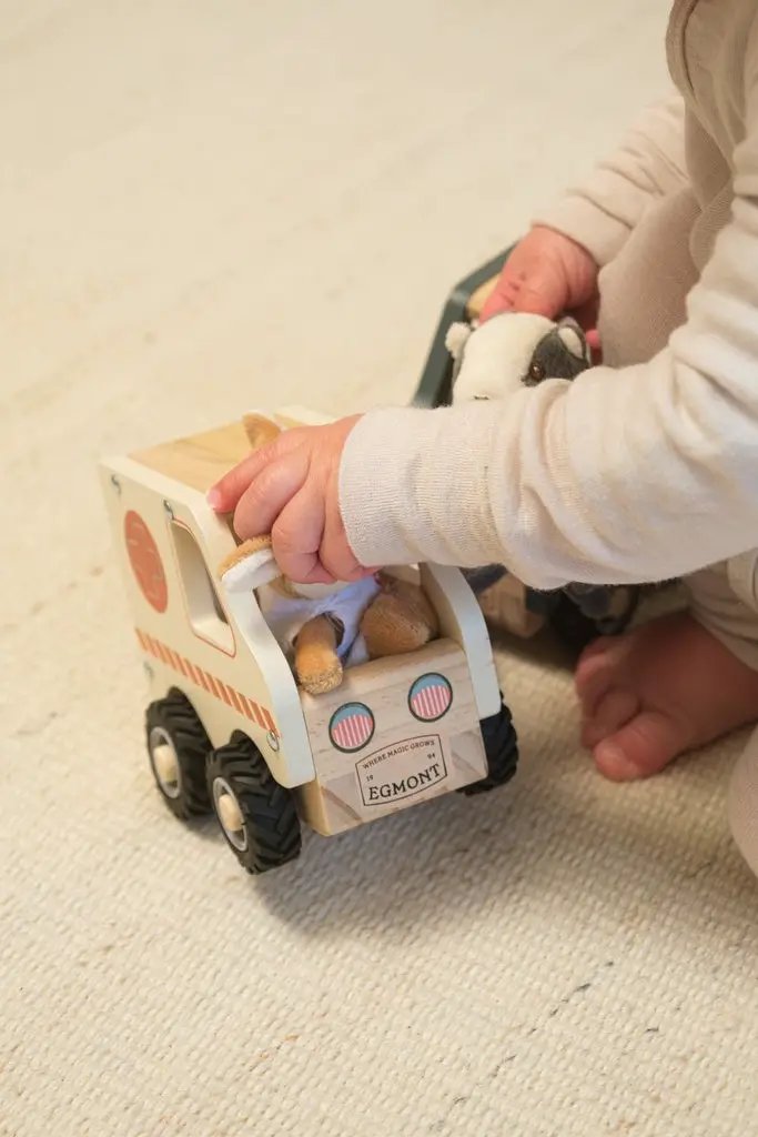 Wooden ambulance toy by EGMONT; white with orange stripe, plush animals inside, four wheels.