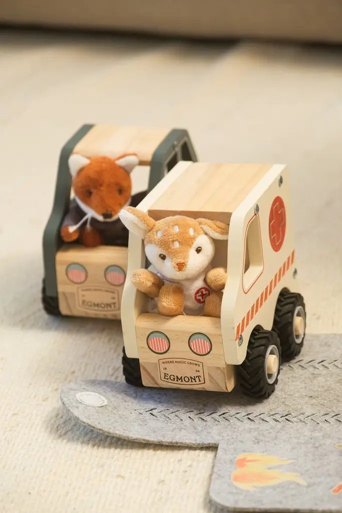 Two wooden EGMONT ambulance toy trucks with fox and fawn plush drivers, natural wood with red accents.