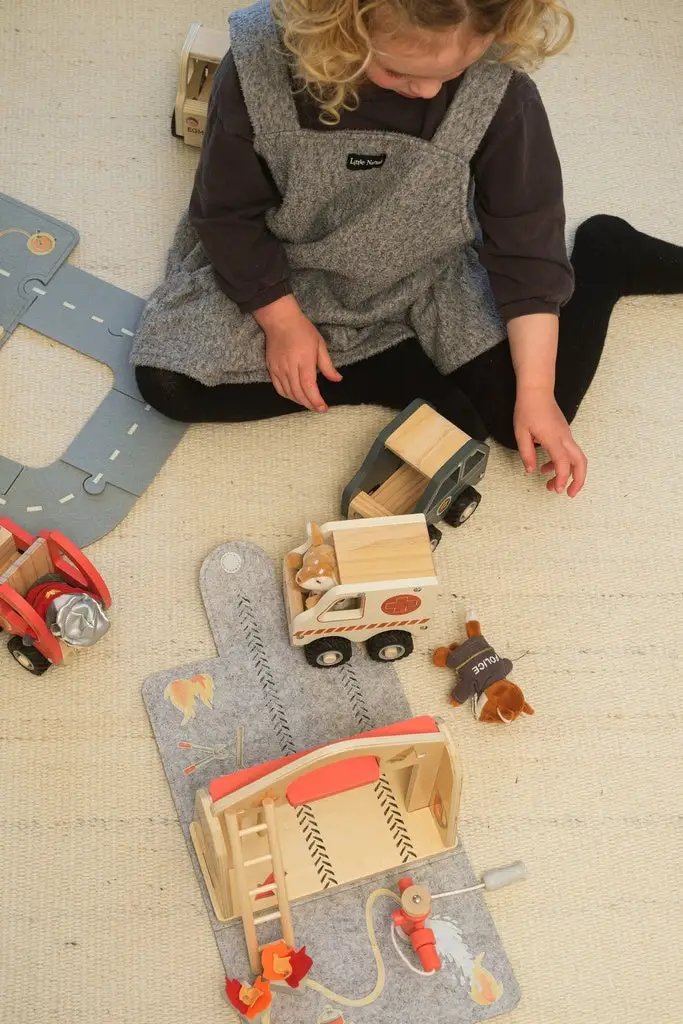Egmont Toys wooden ambulance and construction vehicles set on a beige play mat with a child playing nearby