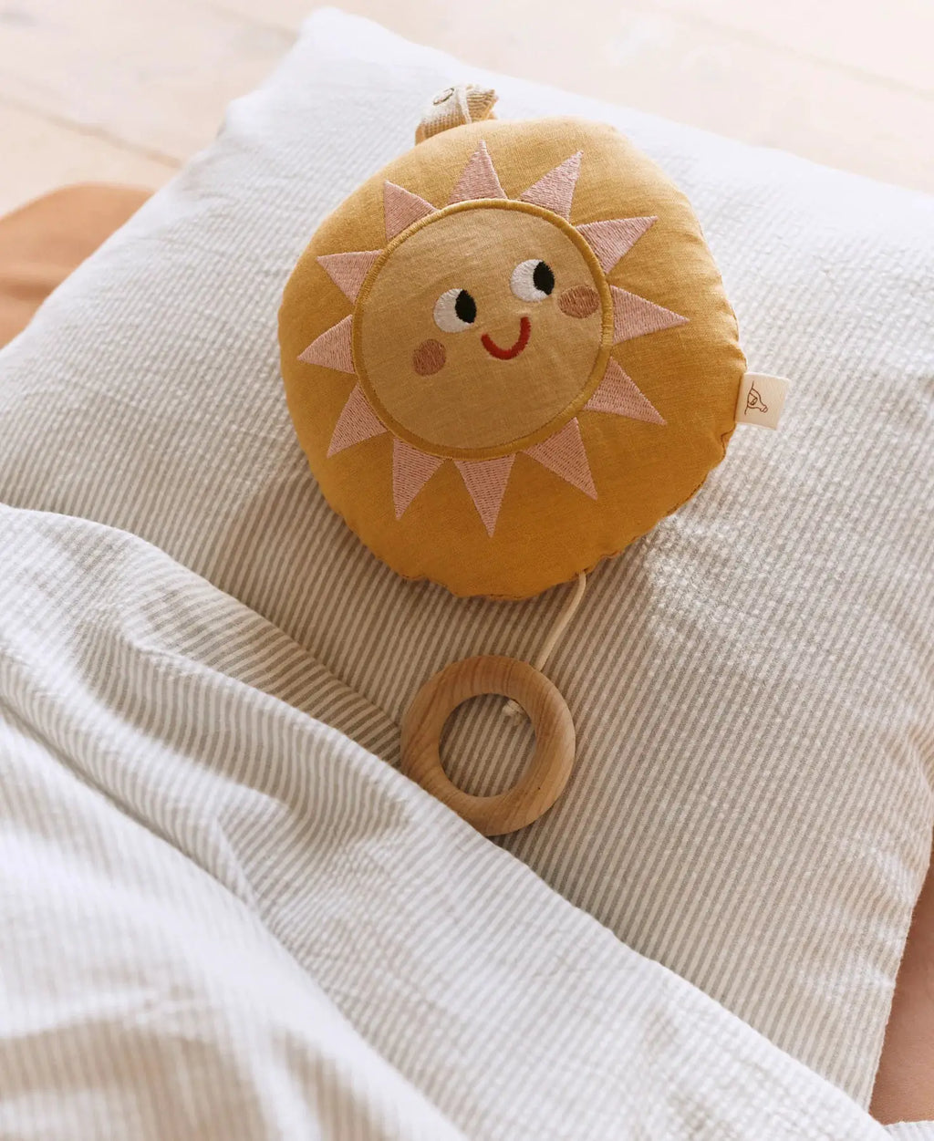 Sun-shaped baby mobile plush in warm yellow with pink rays; wooden ring toy included