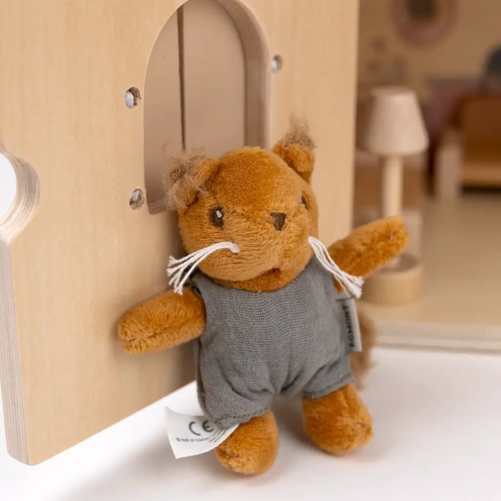 Brown squirrel plush toy in gray fabric overalls attached to a wooden dollhouse panel