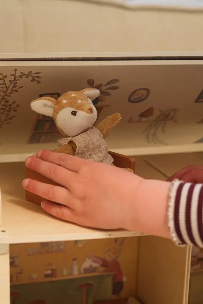 EGMONT TOYS café et boulangerie plush deer in a brown box, being held by a child's hand on a wooden play kitchen shelf