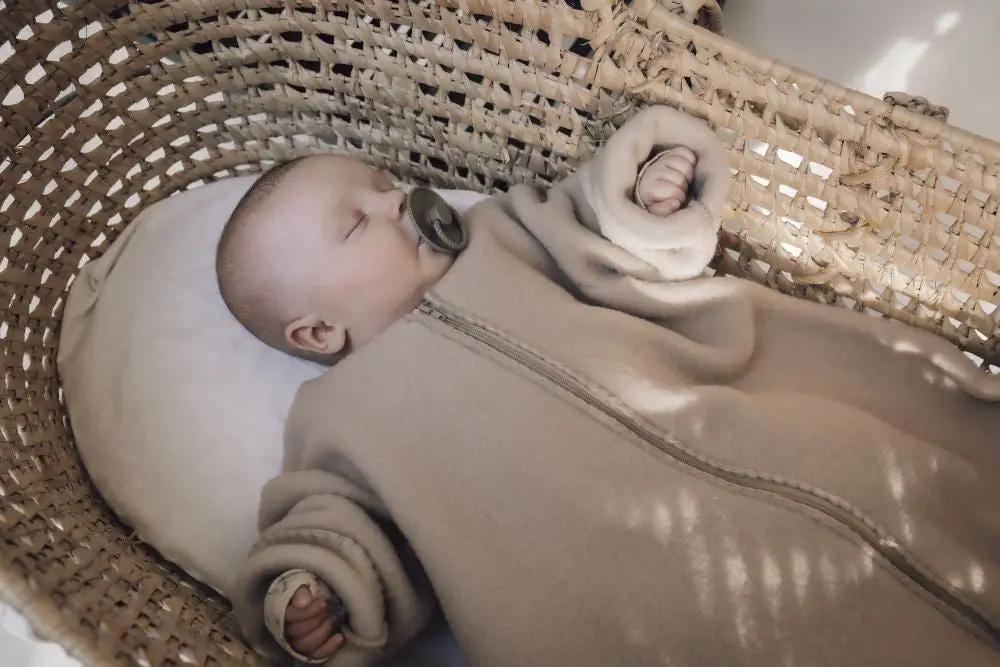 ALWERO gigoteuse en mérinos beige avec manches pour bébé, posé dans un couffin en osier