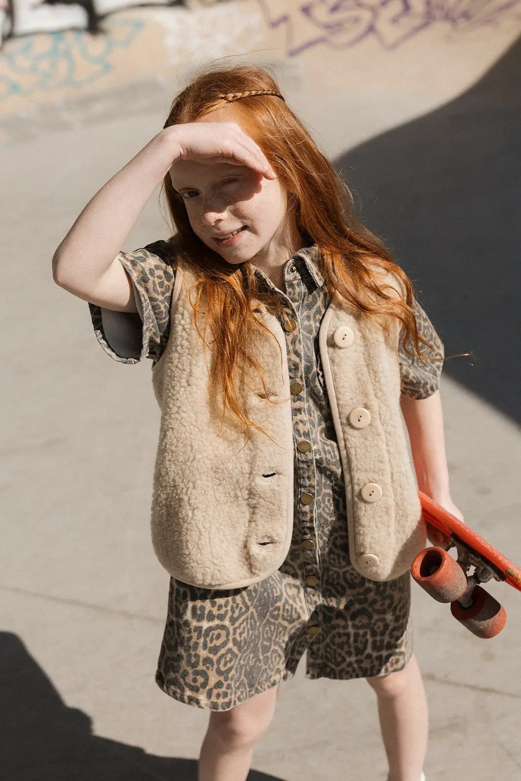 Gilet sans manches ALWERO en laine sand brown, boutons, porté par une jeune fille en robe léopard et skateboard rouge.