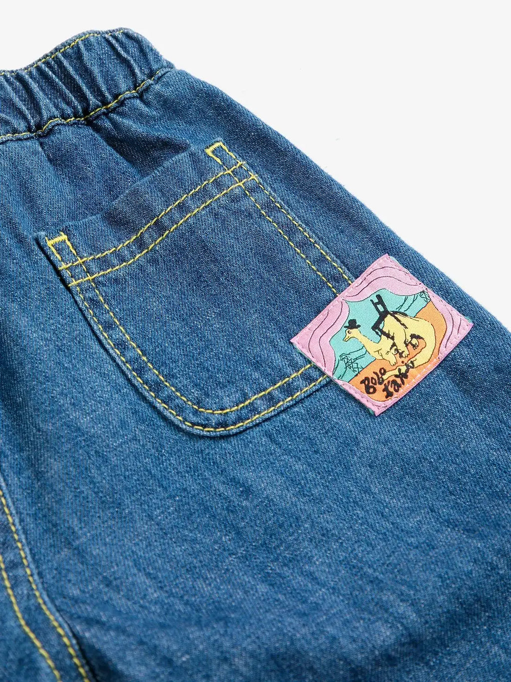 Pantalon denim BOBO CHOSES taxi saurus bleu avec surpiqûres jaunes et patch rose sur la poche arrière