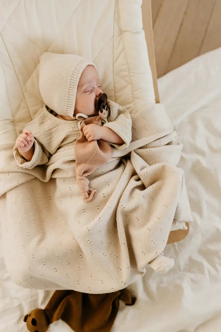 HVID bonnet dolly, cream knit baby hat by Citron Grenadine on a cream blanket.