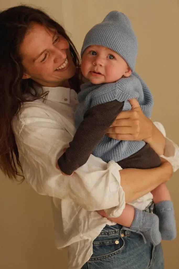 HVID newborn bonnet sky blue; knitted baby hat worn by a baby held by mother