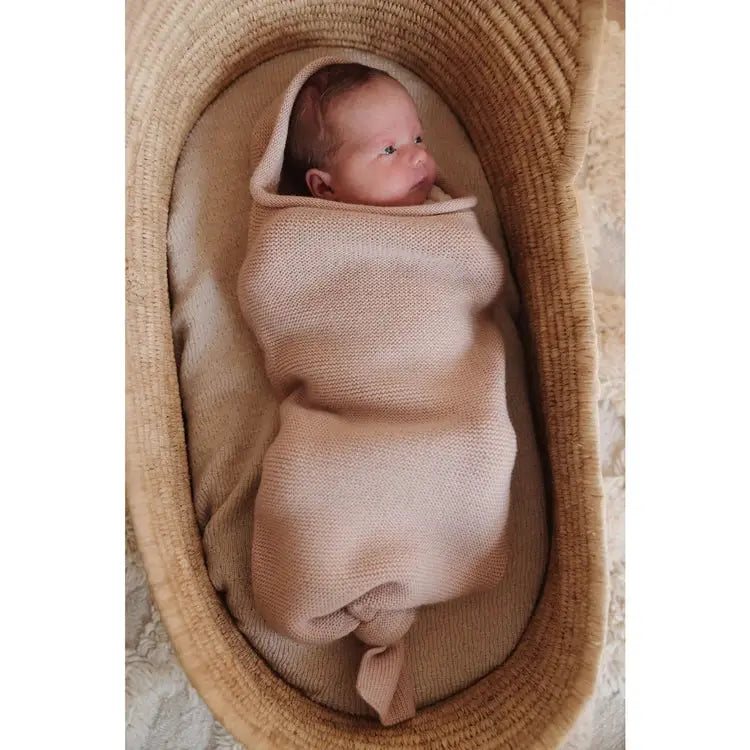 HVID cocoon apricot swaddling blanket from Citron Grenadine; baby wrapped in knit cocoon inside a woven basket