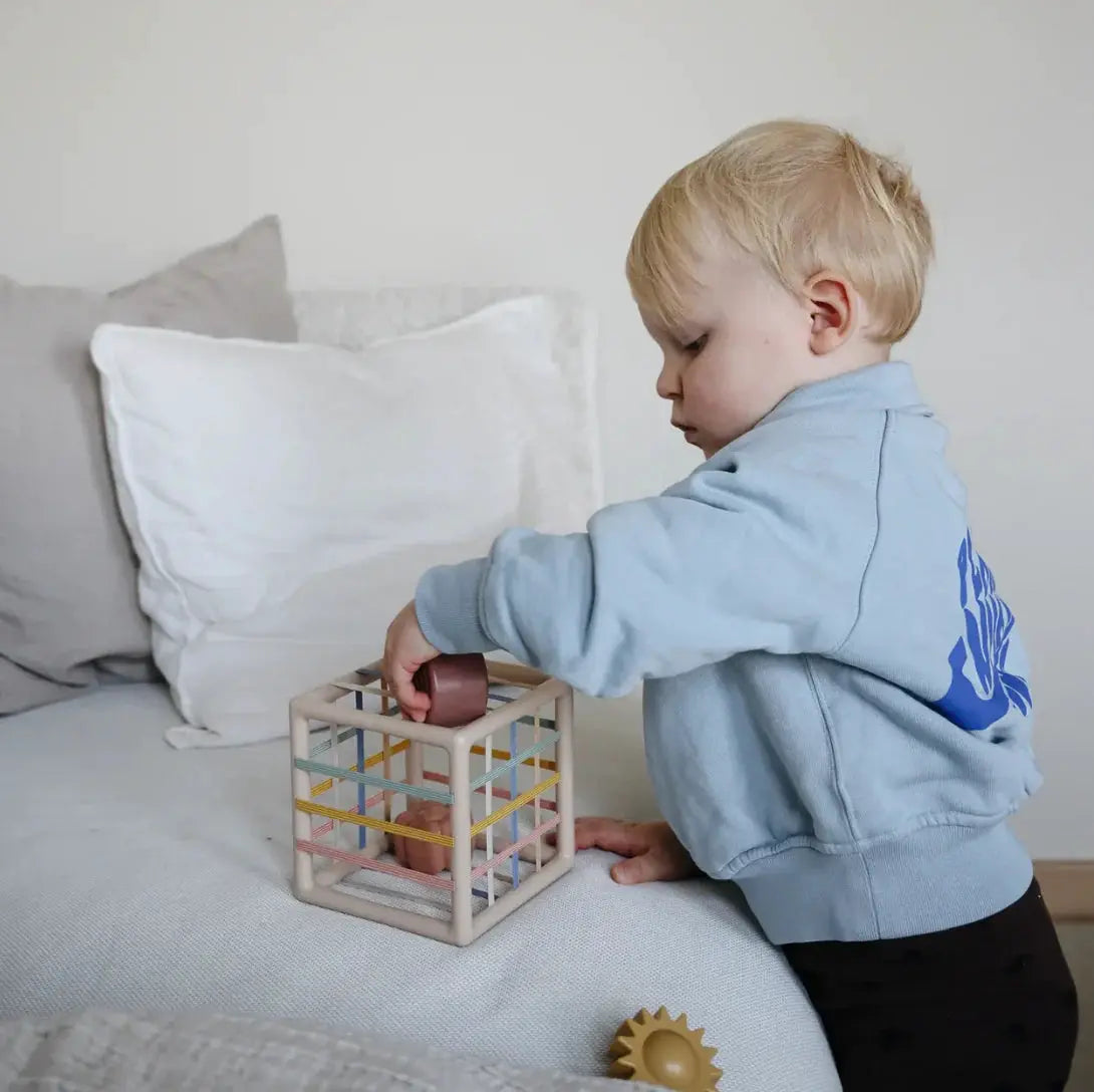 MUSHIE boite à formes et élastiques: cube en cadre bois clair avec bandes colorées, enfant joue