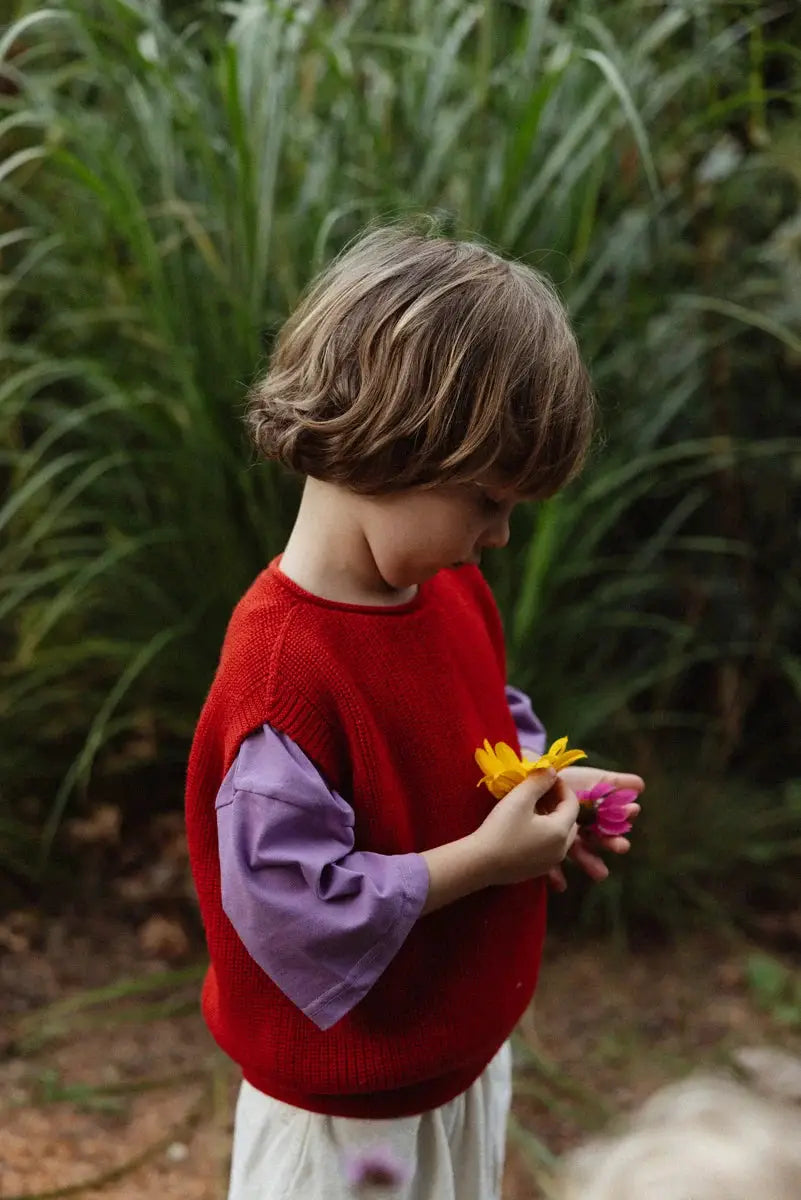 Red knit kids' pullover by Citron Grenadine; child in lavender shirt holding yellow and pink flowers