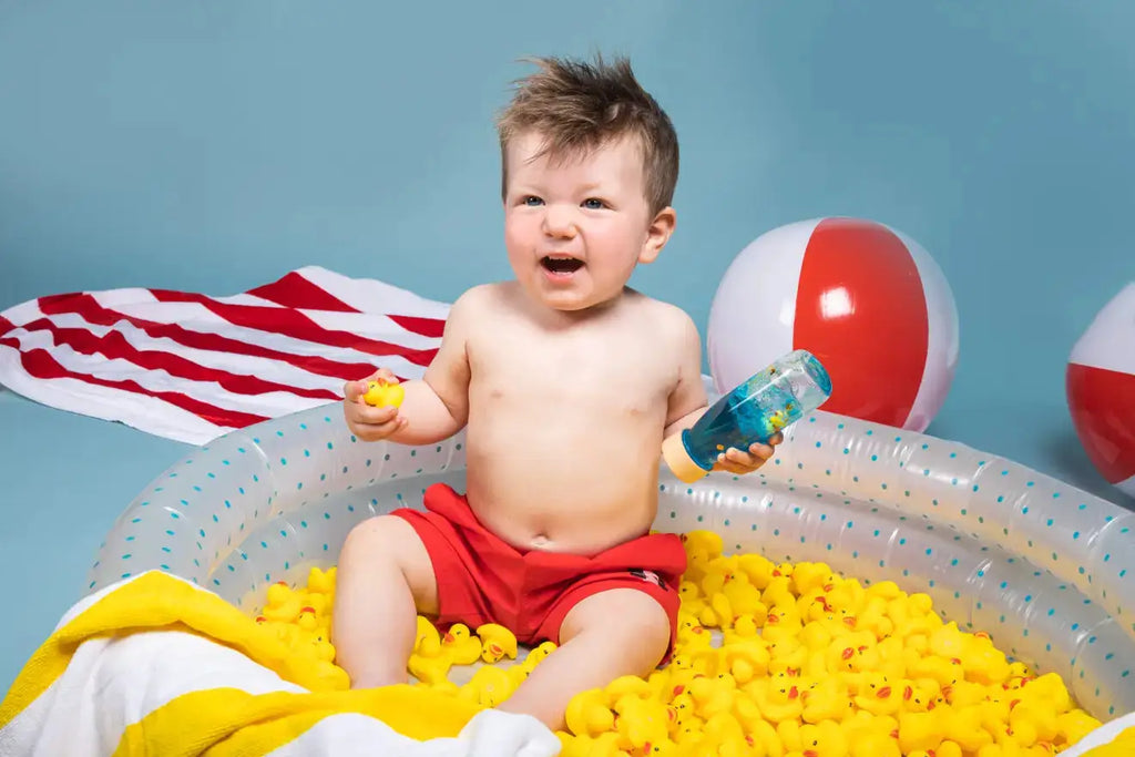 PETIT BOUM bouteille sensorielle; jouet d'éveil Citron Grenadine, bébé entouré de plusieurs canards jaunes dans bassin.