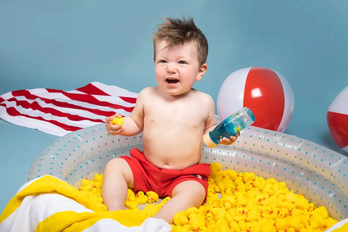 PETIT BOUM bouteille sensorielle; jouet d'éveil Citron Grenadine, bébé entouré de plusieurs canards jaunes dans bassin.
