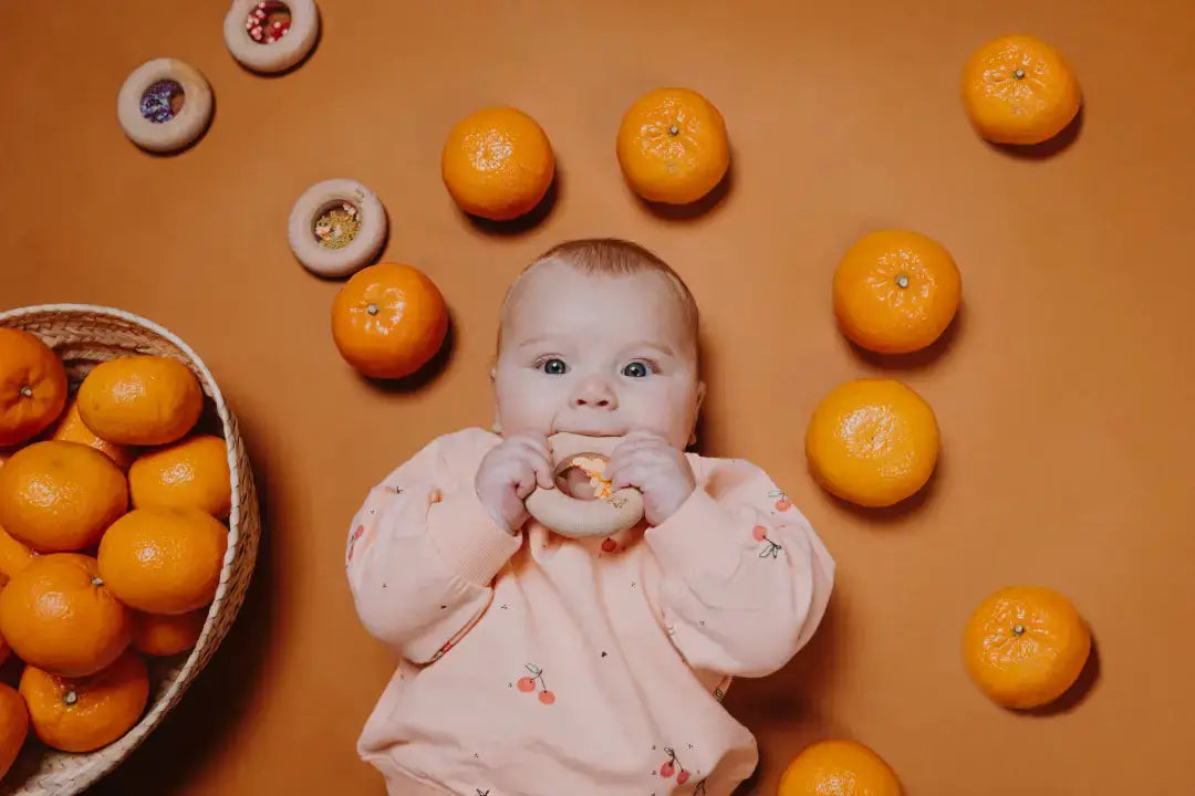 PETIT BOUM donut sensoriel teething toy, beige ring; baby chews surrounded by oranges.