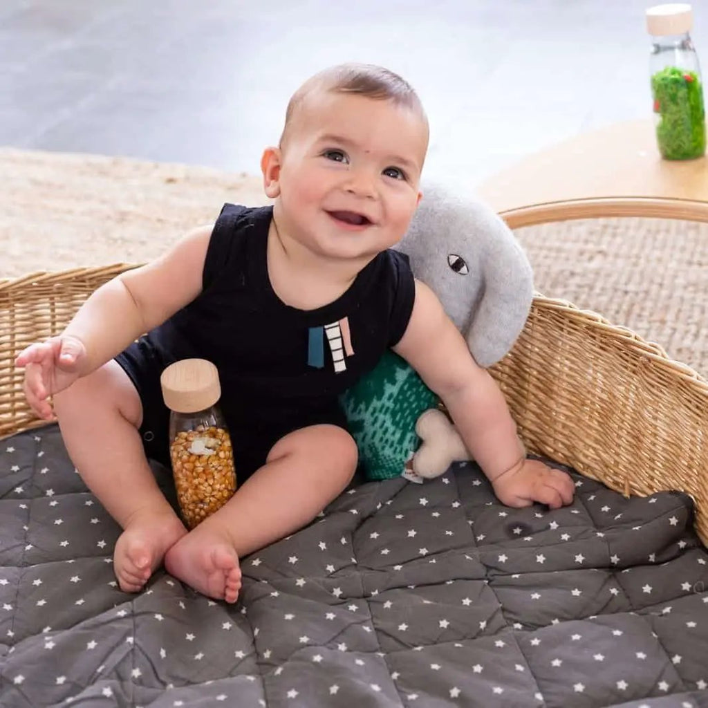 PETIT BOUM bouteille sensorielle farm; spy bottle avec graines, bébé sur un tapis, bouteille à l’arrière-plan