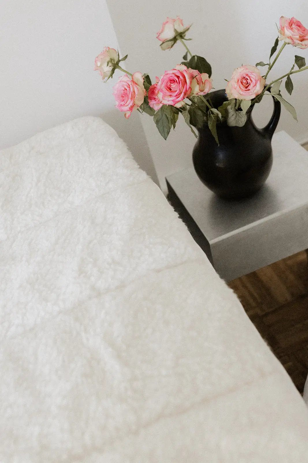 Surmatelas Coni laine et coton blanc, vase noir et roses sur une table de chevet grise