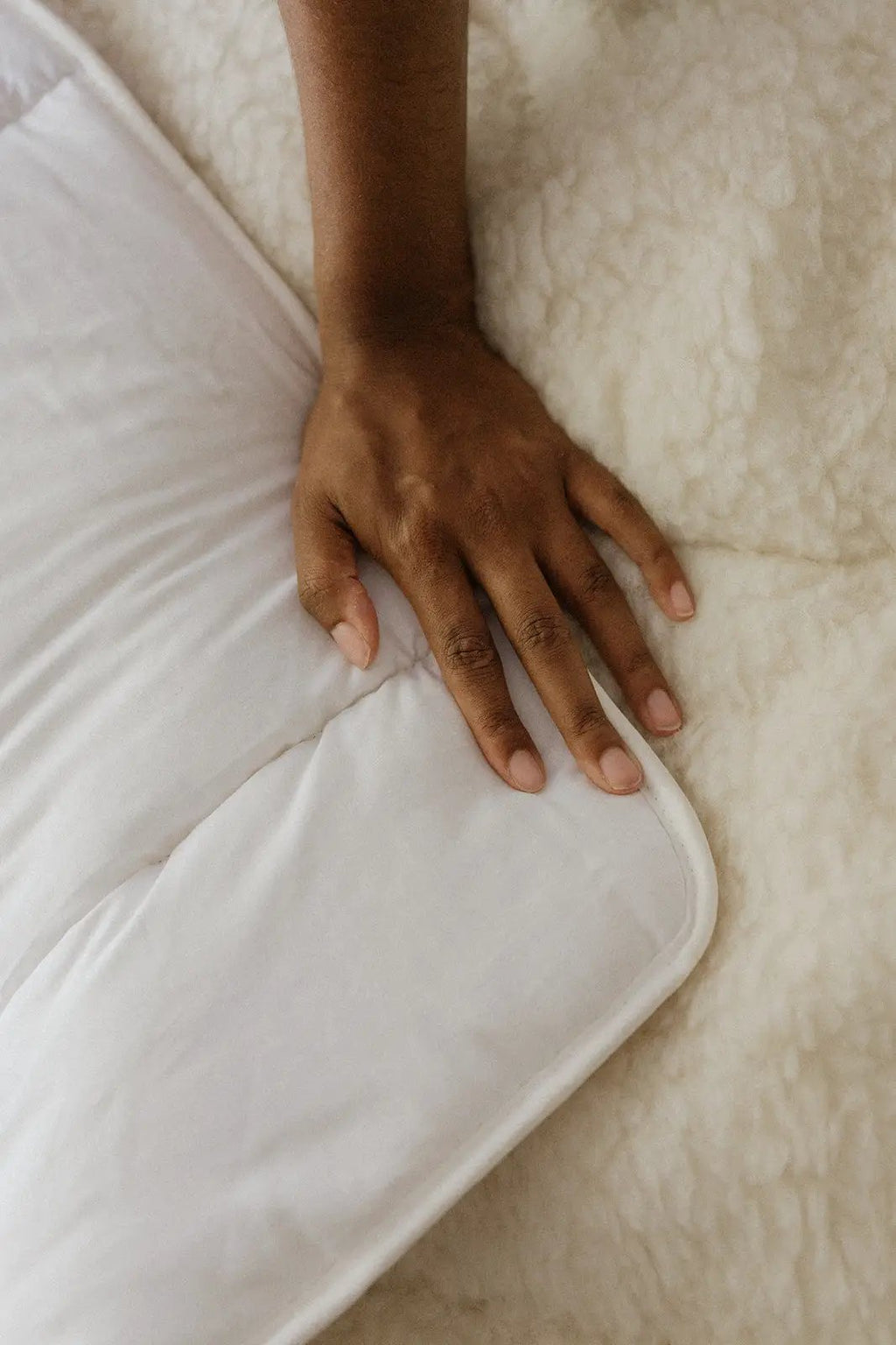 Surmatelas blanc en laine et coton, main posant sur le bord, texture douillette sur fond crème.