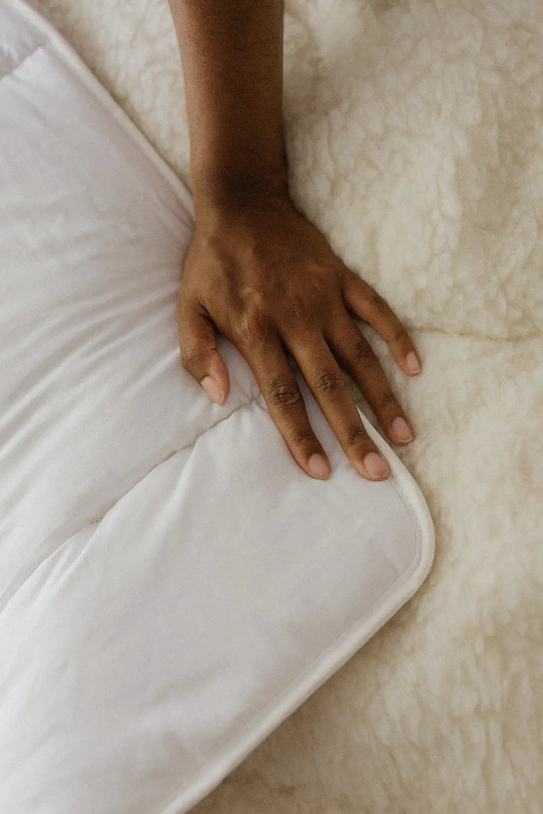 Surmatelas blanc en laine et coton, main posant sur le bord, texture douillette sur fond crème.