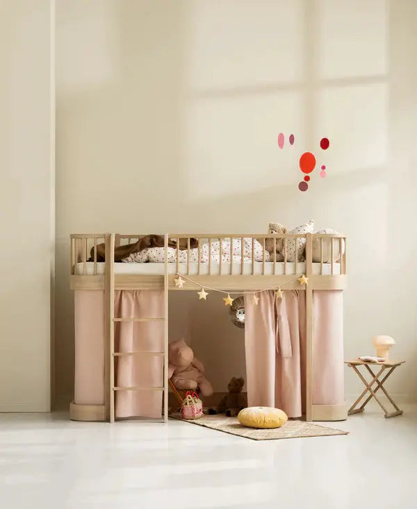 Oliver Furniture loft bed in natural oak with pink curtains, ladder on left, star garland and toy-filled space underneath.