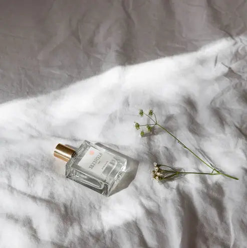 MINOIS eau de toilette by Citron Grenadine; clear glass bottle with gold cap on white fabric, with small flowers.