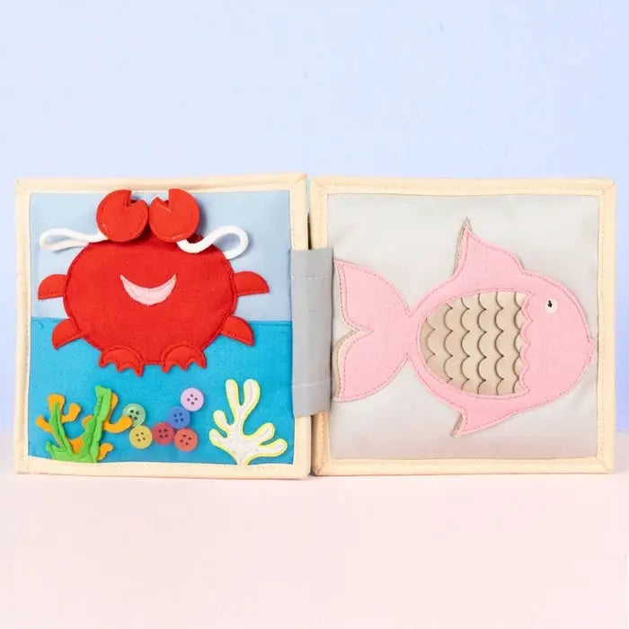 JOLLY DESIGNS livre d'éveil bébé en tissu, crab rouge et poisson rose sur fond bleu avec coraux