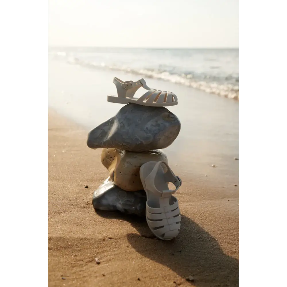 LIEWOOD baby sandals in sandy beige perched on stacked beach rocks
