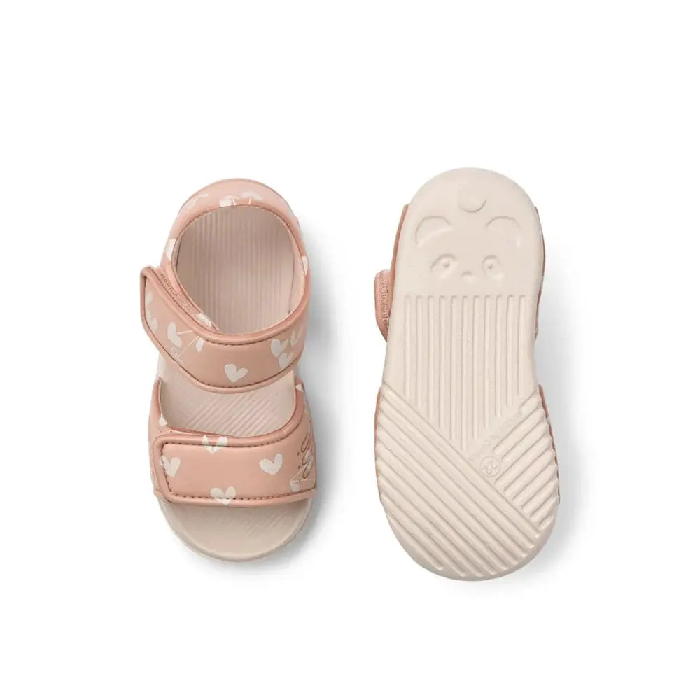 Pair of pink baby sandals with white heart pattern, two Velcro straps and pale beige sole.