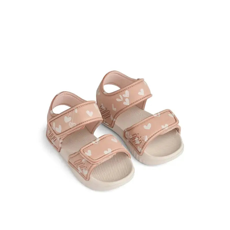 Pair of pale pink kids' sandals with white heart patterns and Velcro straps