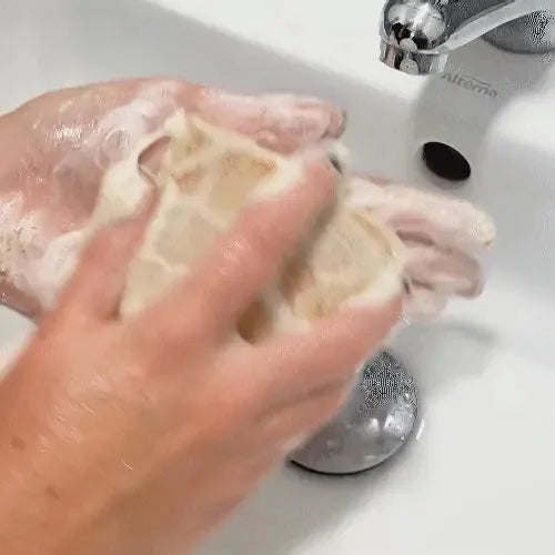 Savon COMME AVANT au beurre de karité, savon solide rose pâle en mousse près du robinet.