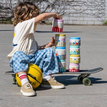 THE COTTON CLOUD thermos lunch box inox 350ml on skateboard scene with a child beside colorful stackable cups outdoors