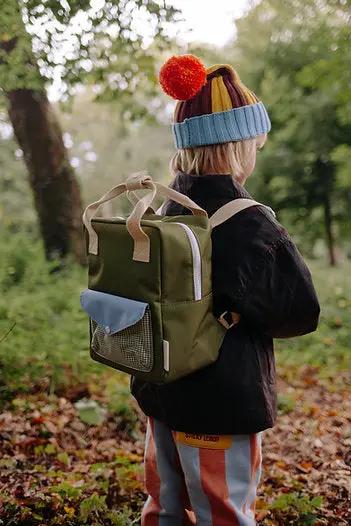 Citron Grenadine sac à dos scolaire vert olive avec poche frontale bleue et sangles beige, porté par un enfant en forêt
