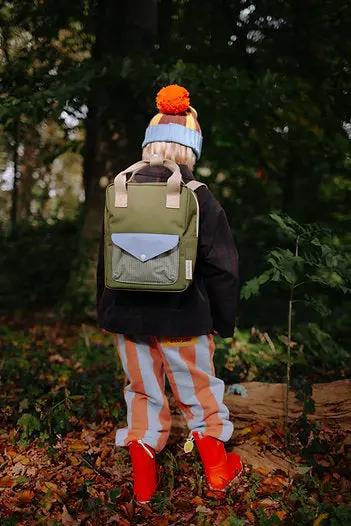 Sac à dos scolaire Citron Grenadine Sticky Lemon en vert olive avec rabat bleu clair, porté par un enfant dans une forêt