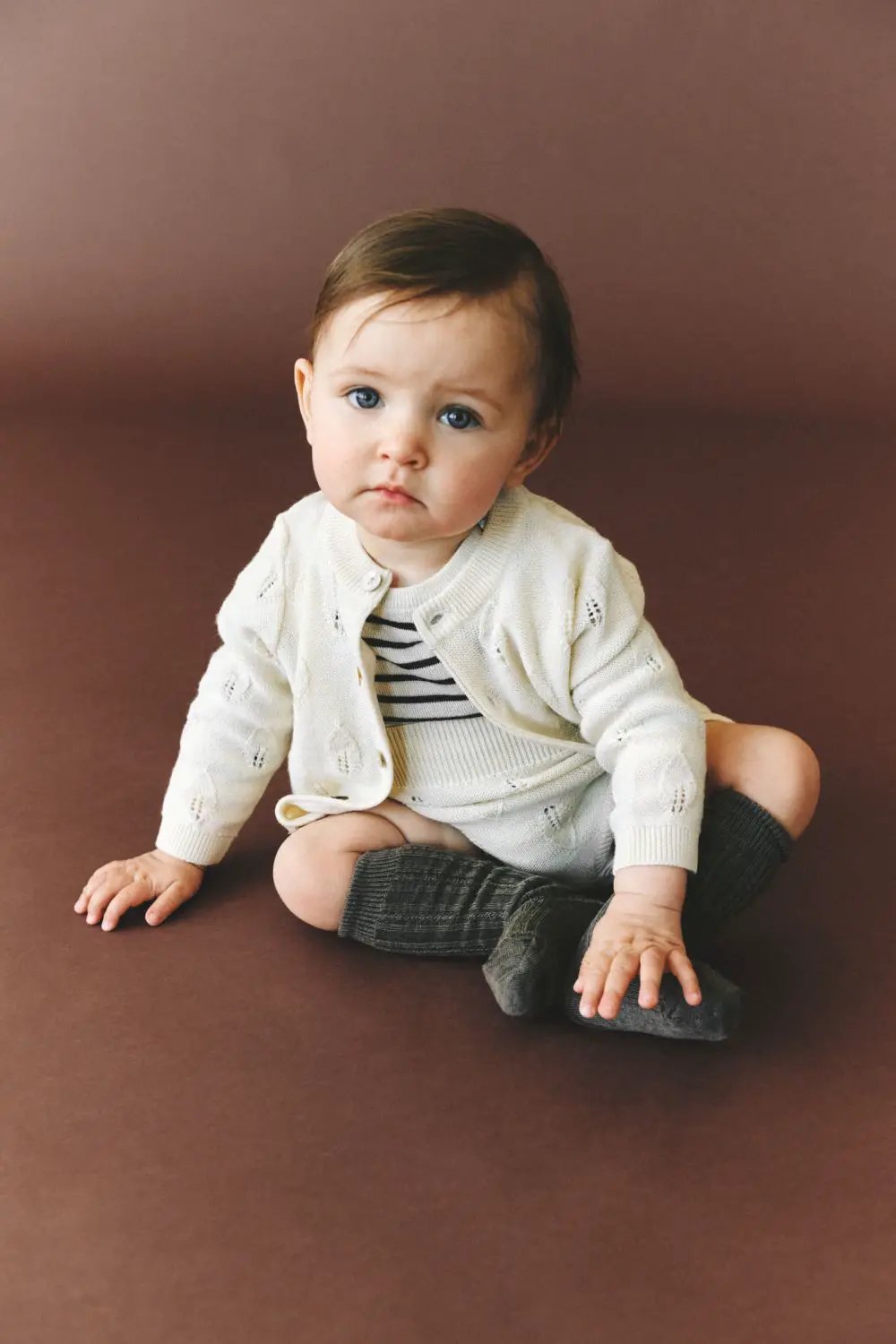 FUB body en merinos écru et navy pour bébé, assis sur fond brun, cardigan crème et chaussettes gris.