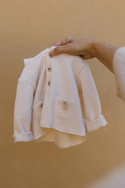 Gilet Dunkerque écru en maille avec boutons front et poche, tenu par une main