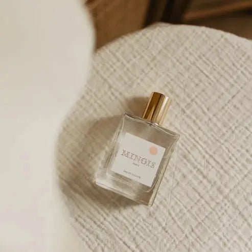 MINOIS eau de toilette by Citron Grenadine, glass bottle with gold cap on a textured beige surface