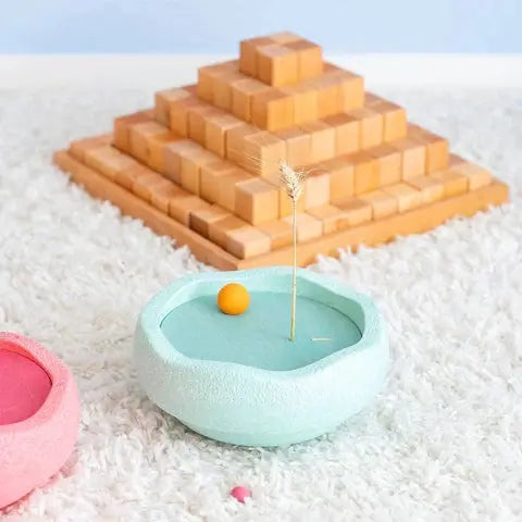 Stapelstein x Grimms Rolling Discs set in cool pastel; teal bowl with orange ball beside stacked wood blocks.